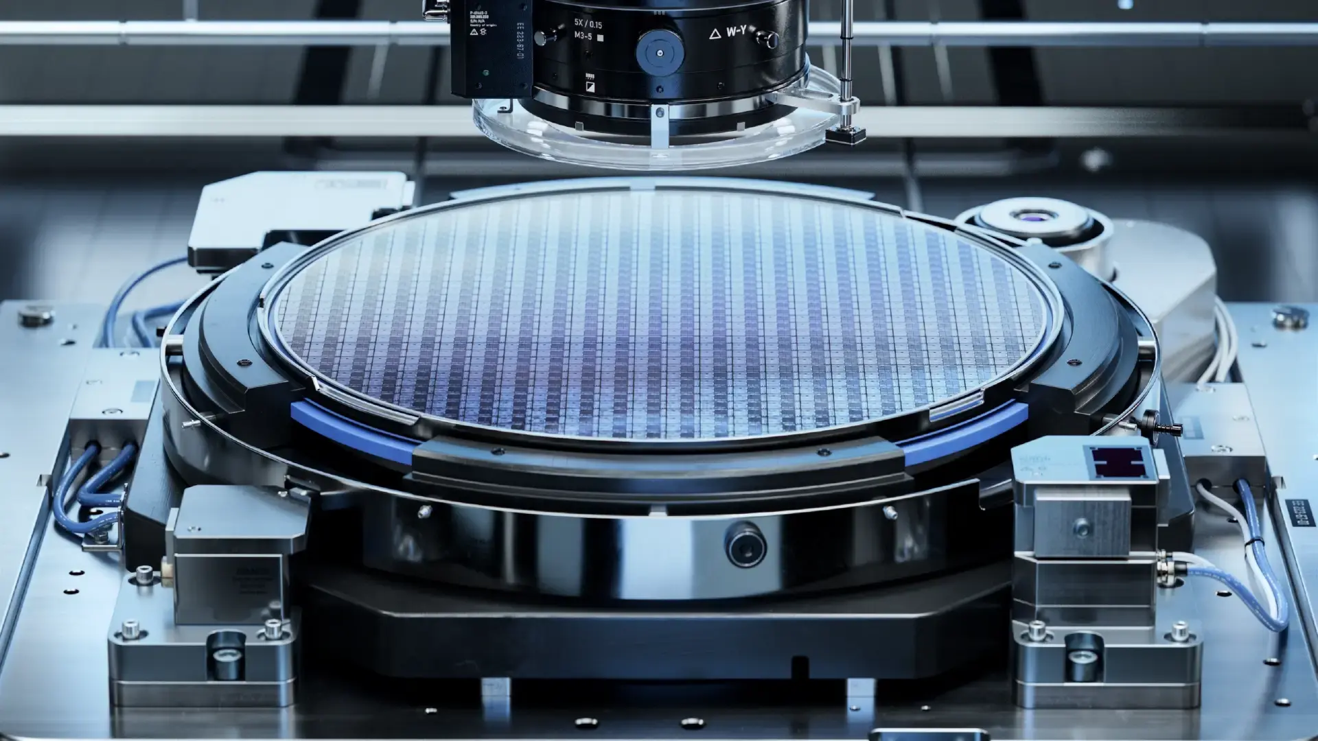 Close-up of a circular metallic plate with a grid pattern mounted on a mechanical device, surrounded by components and sensors, representing precision engineering.